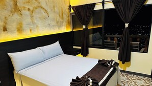 Ein Hotelzimmer mit Bett, Vorhängen, Nachtblick durch das Fenster und einem gemusterten Boden.