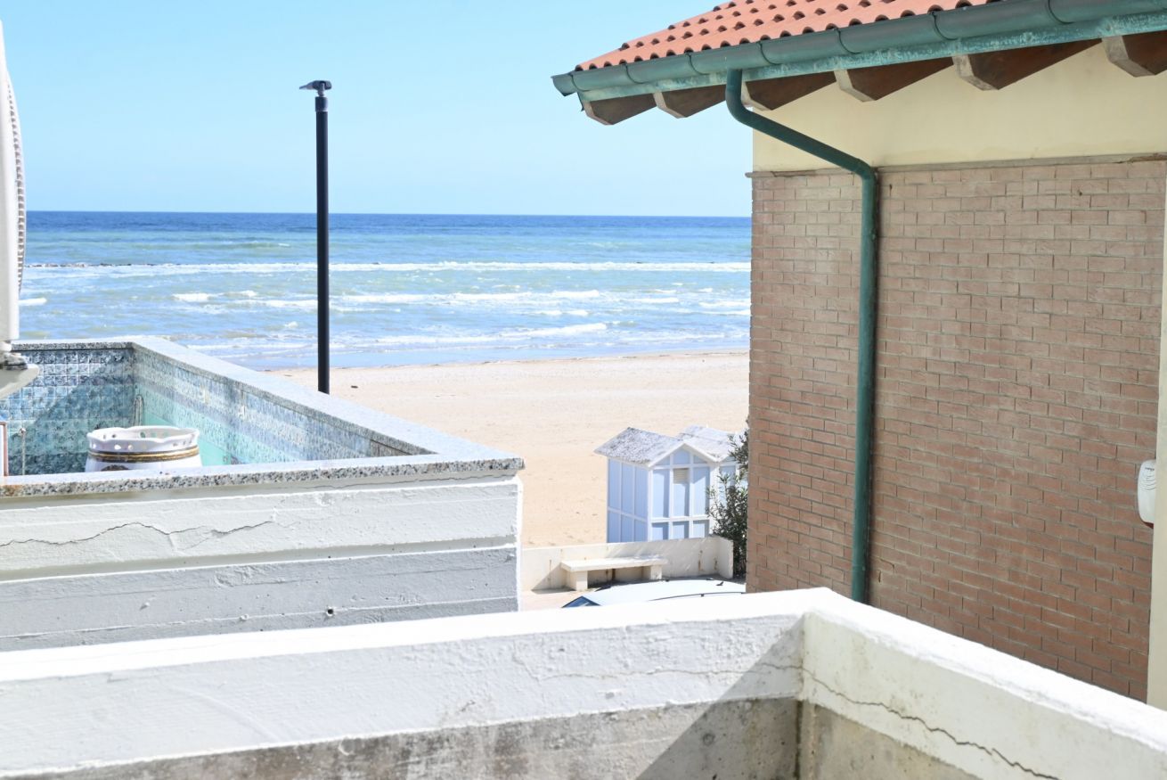 A beach view from a balcony with a pool, a brick wall, and a clear sky.