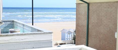 A beach view from a balcony with a pool, a brick wall, and a clear sky.