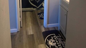 A hallway with a shower curtain featuring a Vegas Raiders logo, a small towel rack with a patterned towel, and a doormat with the same logo. - Cozy Guest Retreat for 8 Near The Strip! (North Las Vegas)