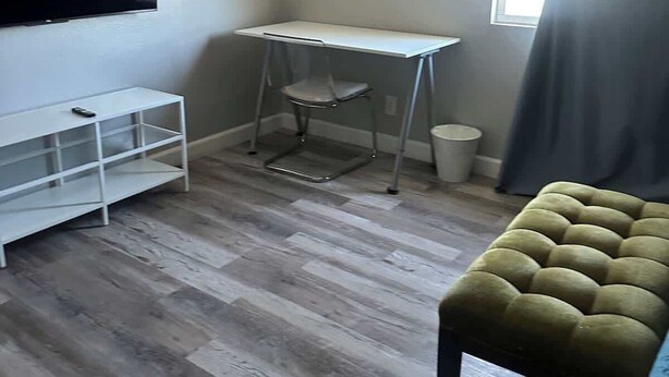 A room with a TV mounted on the wall, a white desk, a cushioned bench, and a window with curtains. - Cozy Guest Retreat for 8 Near The Strip! (North Las Vegas)