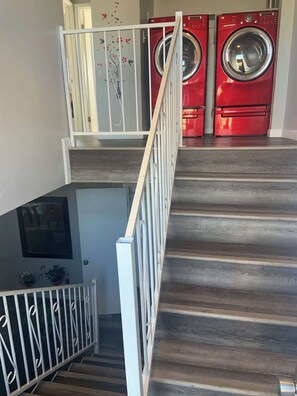 Eine Treppe mit Geländer führt zu einem Waschraum mit zwei roten Waschmaschinen.