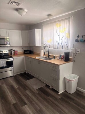 A modern kitchen with white cabinets, a stainless steel stove, a sink, and a window with a floral curtain. - Charming Vegas Getaway | Minutes from The Strip (North Las Vegas)