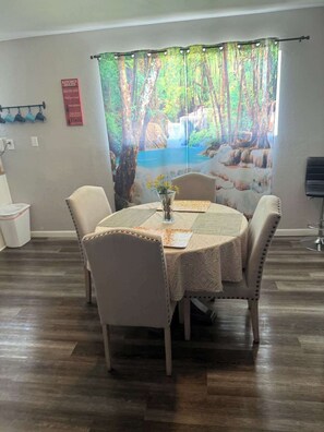 A dining area with a round table, four chairs, a vase with flowers, a kitchen rules poster, and a forest-themed curtain. - Charming Vegas Getaway | Minutes from The Strip (North Las Vegas)