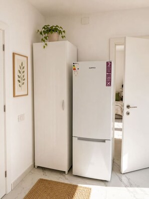A compact kitchen with two white appliances, a door with a lock, and a framed plant on the wall. - Deluxe Two-Bedroom Apartment with Balcony (Bucharest)
