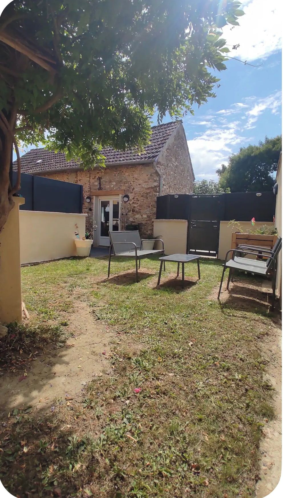 A backyard with a stone building, a covered seating area, and a barbecue grill.