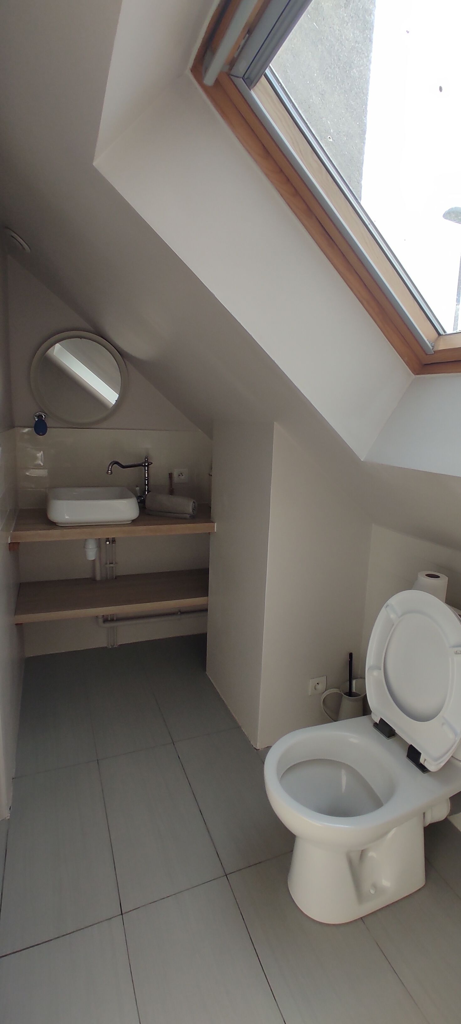 Un baño pequeño con tragaluz, inodoro, lavabo y espejo.