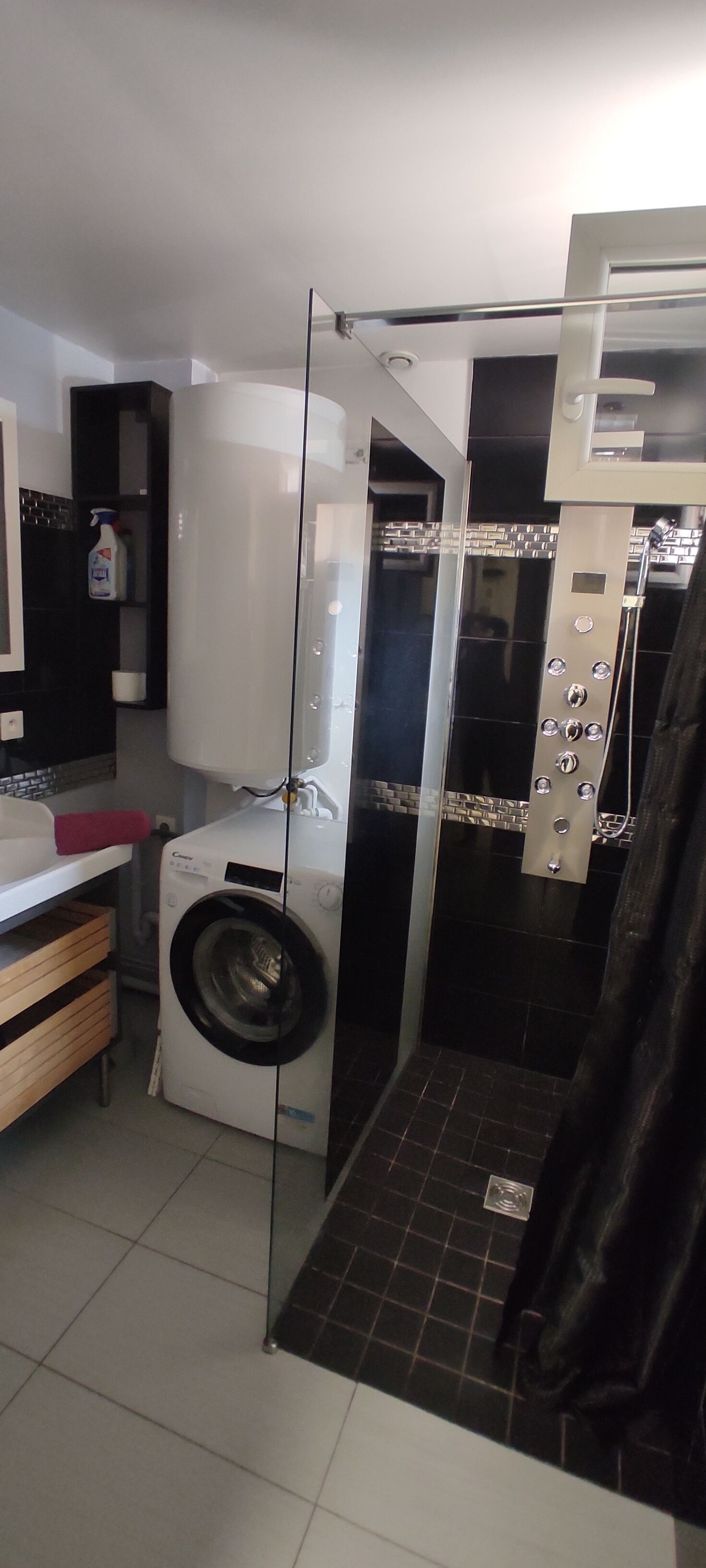 Een kleine badkamer met een wasmachine, een douchecabine van glas en een toilet.