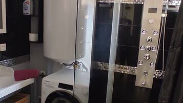 Een kleine badkamer met een wasmachine, een douchecabine van glas en een toilet.