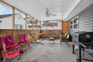 An enclosed patio with a ceiling fan, a grill, and outdoor furniture including folding chairs and a hammock.