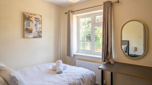 Ein Schlafzimmer mit einem Bett, einem Fenster mit Vorhängen, einem Heizkörper und einem wandmontierten Spiegel.