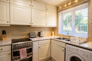 A kitchen with white cabinets, a stainless steel stove, a washing machine, and a window with blinds. - 2-Bed House Sleeps 6 with Parking · 12 Min Walk to Nottingham Castle (Nottingham)