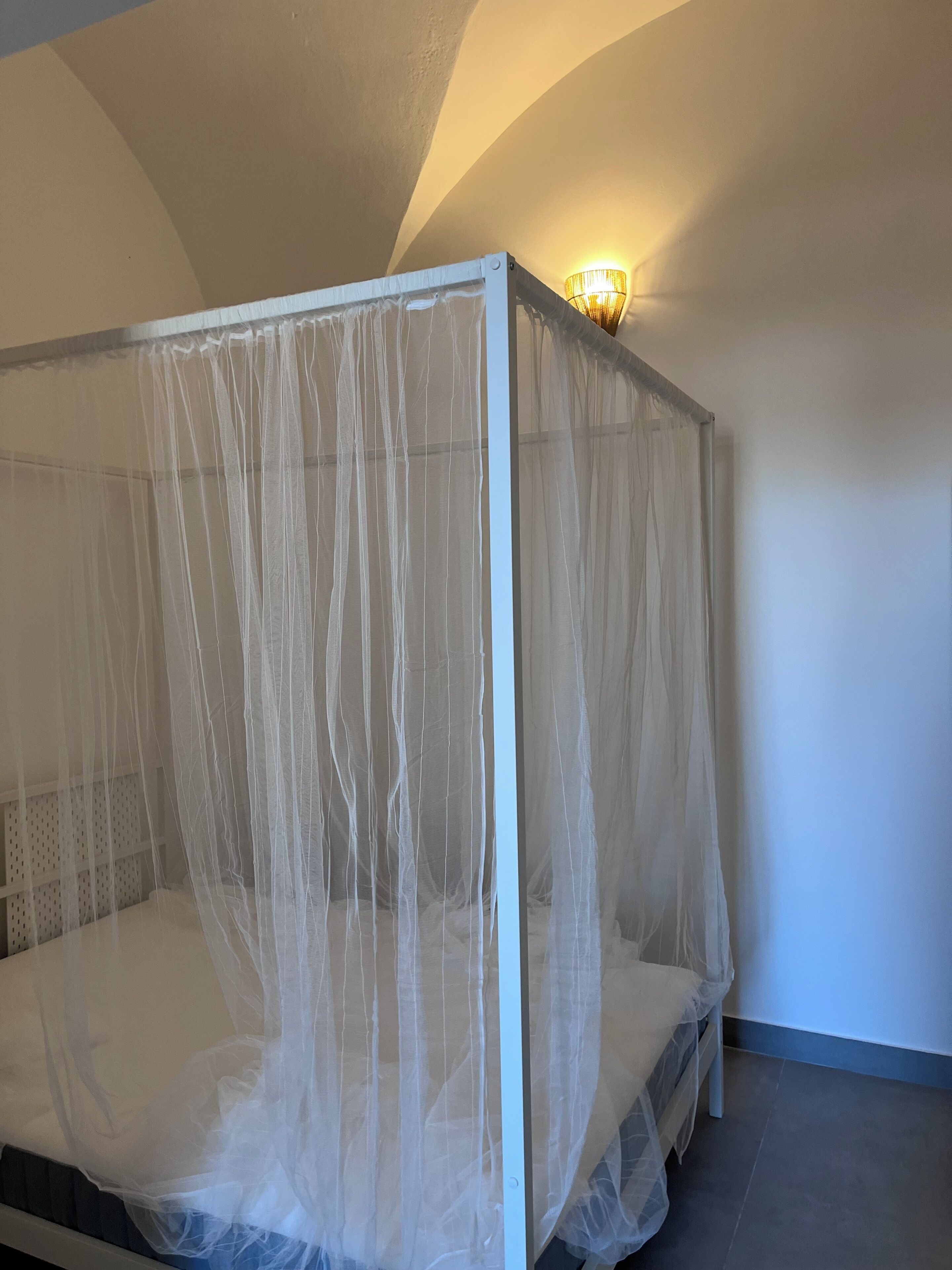 Un lit à baldaquin à quatre poteaux, un luminaire fixé au mur et un sol carrelé.