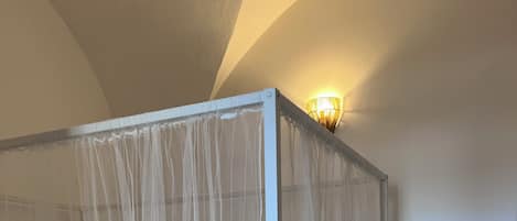 A four-poster bed with a sheer canopy, a wall-mounted light fixture, and a tiled floor.
