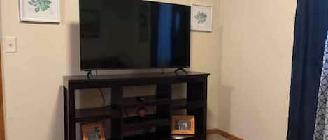A room with a television on a dark wooden stand, two framed pictures on the wall, and a carpeted floor.
