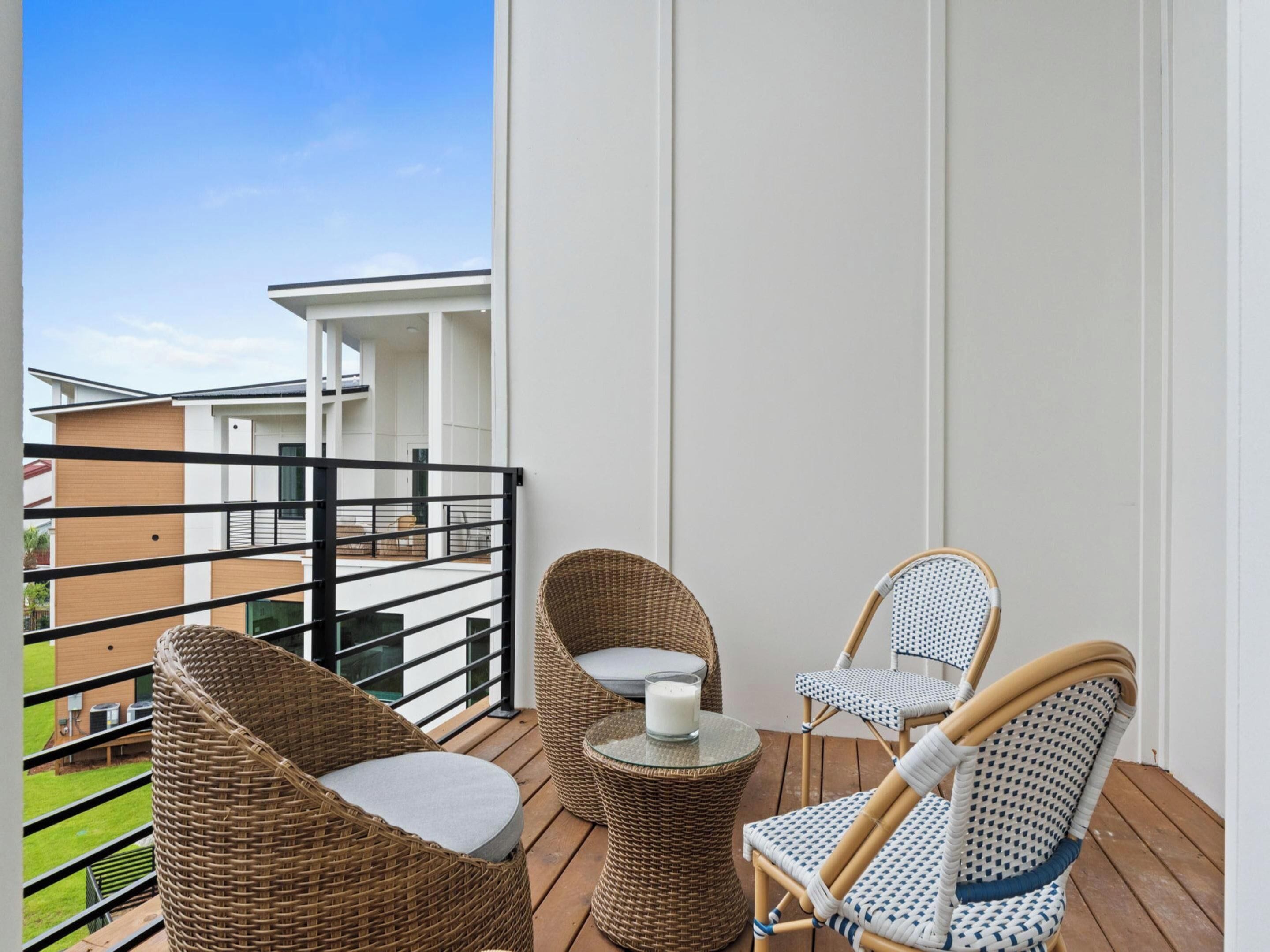 A balcony with wicker furniture, a glass table with a candle, and a view of adjacent buildings.