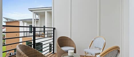 Uma varanda com móveis de vime, uma mesa de vidro com uma vela e vista para edifícios próximos.