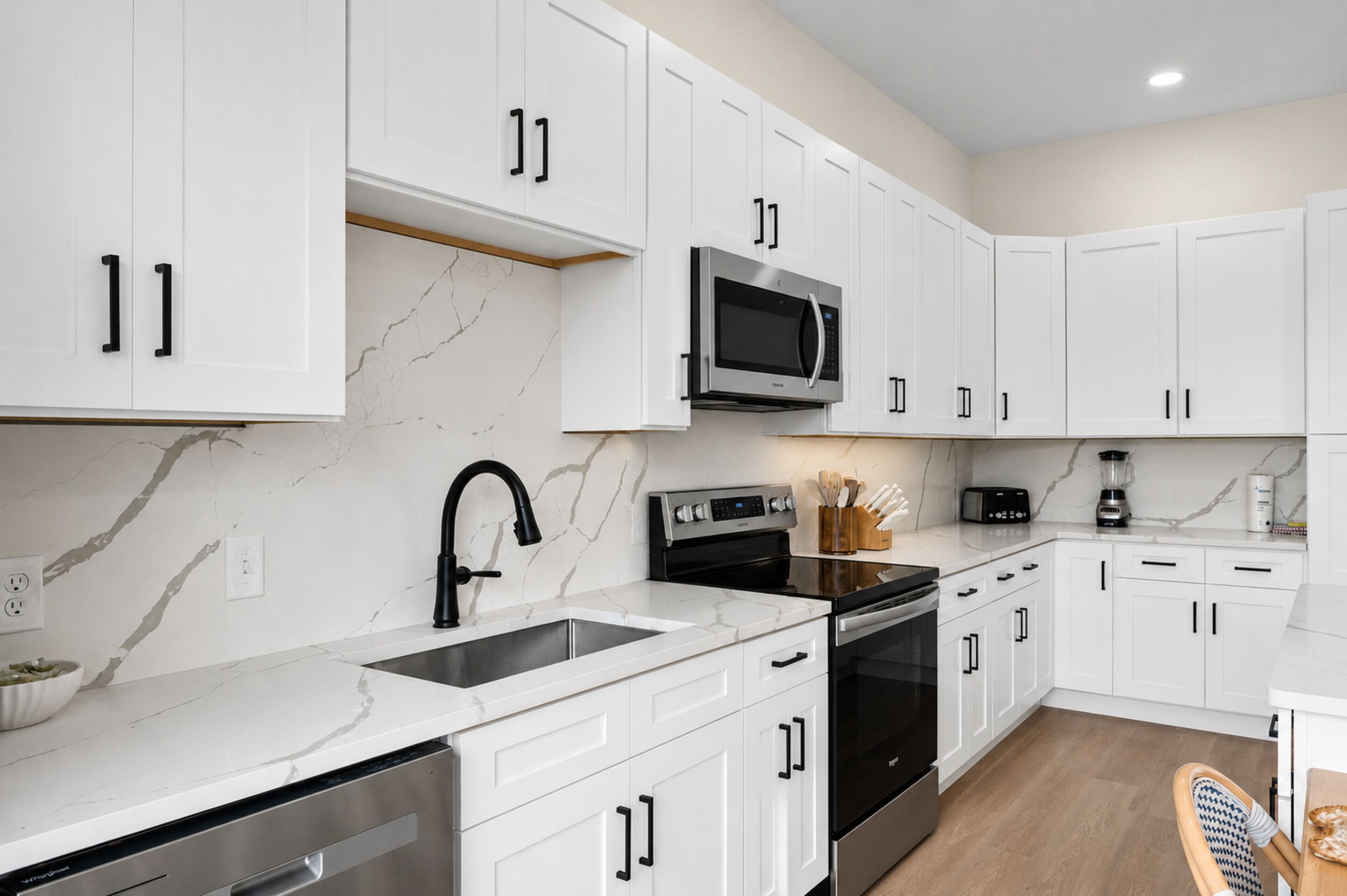 A modern kitchen with white cabinets, a stainless steel sink, a microwave, and a stove.