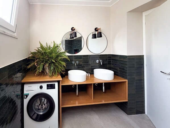 Ein modernes Badezimmer mit Waschmaschine, zwei Waschbecken und einem großen Spiegel.