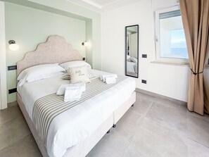 Ein ordentlich bezogenes Bett mit Kissen und Handtüchern, ein großer Spiegel und ein Fenster mit Vorhängen.