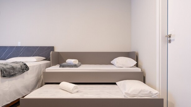 Habitación de hotel con dos camas, una con cabecera y otra sin, ambas con sábanas y almohadas blancas.