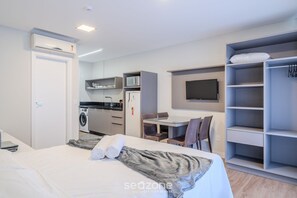 Una habitación de hotel moderna con cama, escritorio, televisor, lavadora y armario.