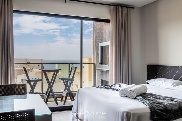 A hotel room with a bed, a table, and chairs, a balcony with a view of buildings and the sea. - Studio w/ Pool & BBQ 300m From Sea Vfr505 (Bombinhas)