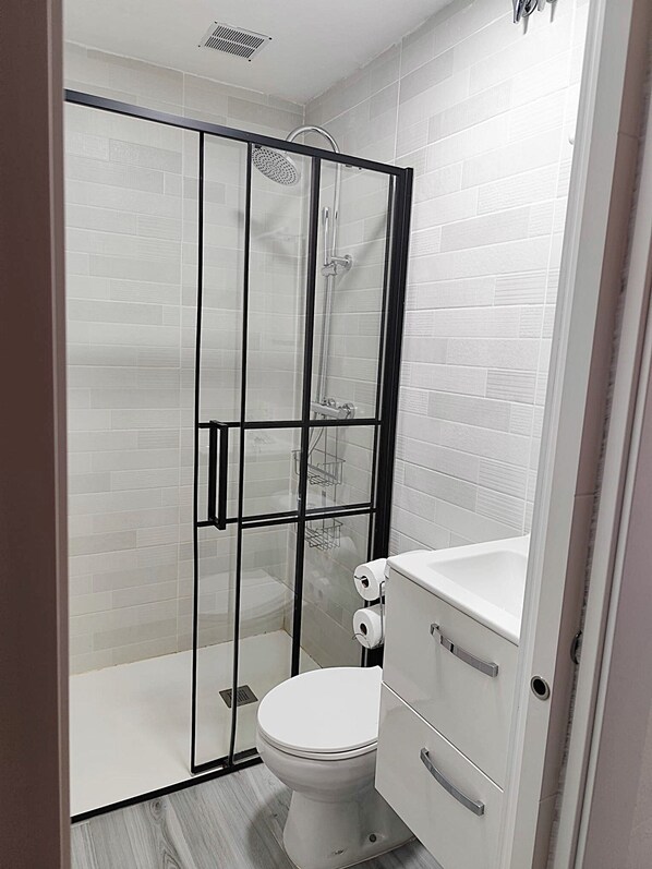Een moderne badkamer met een douche met glazen wand, een wit toilet en een opbergkast.