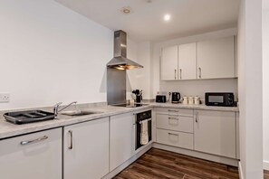 A modern kitchen with white cabinets, stainless steel appliances, and a wooden floor. - Host & Stay | Colquitt Street (Liverpool)
