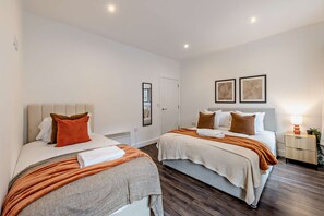 A hotel room with two beds, a bedside table, a nightstand, and a wall-mounted lamp. - Host & Stay | Colquitt Street (Liverpool)