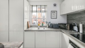 A modern kitchen with white cabinetry, a built-in microwave, and a view of the city. - Stylish 2BDR 2BA Flat with Chic Interiors (West Midlands)