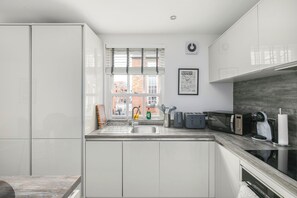 A modern kitchen with white cabinetry, a built-in microwave, and a view of the city. - Stylish 2BDR 2BA Flat with Chic Interiors (West Midlands)