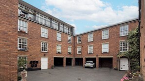 A courtyard with a car parked in a garage, surrounded by brick buildings with multiple windows and balconies. - Stylish 2BDR 2BA Flat with Chic Interiors (West Midlands)