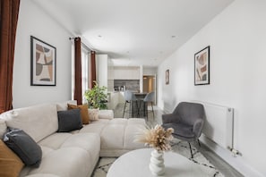 A modern living room with a sectional sofa, a grey armchair, and a white vase with dried flowers. - Stylish 2BDR 2BA Flat with Chic Interiors (West Midlands)