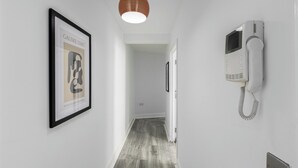 A hallway with a framed artwork on the left, a white telephone on the right, and a hanging pendant light. - Stylish 2BDR 2BA Flat with Chic Interiors (West Midlands)