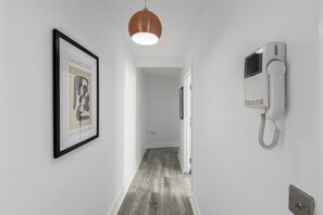 A hallway with a framed artwork on the left, a white telephone on the right, and a hanging pendant light. - Stylish 2BDR 2BA Flat with Chic Interiors (West Midlands)