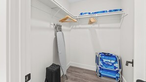 Ein kompakter Raum mit weißer Wand, einem Wäscheständer aus Holz, einem weißen Handtuch, einem blauen Koffer und einem Rollstuhl.
