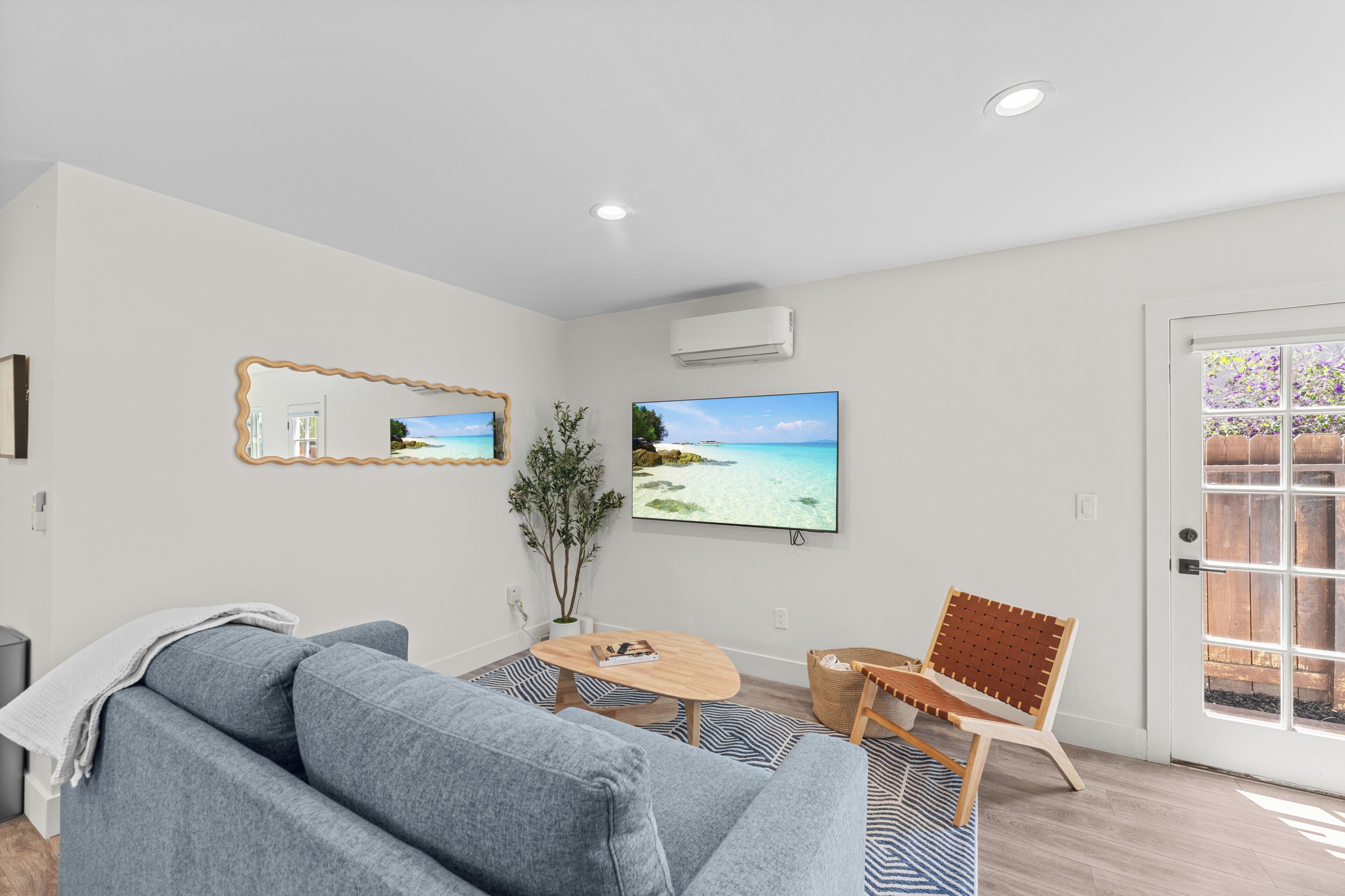 A modern living room with a grey sofa, a wooden coffee table, and a large flat-screen TV mounted on the wall.