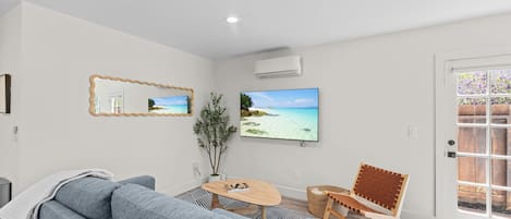 A modern living room with a grey sofa, a wooden coffee table, and a large flat-screen TV mounted on the wall.