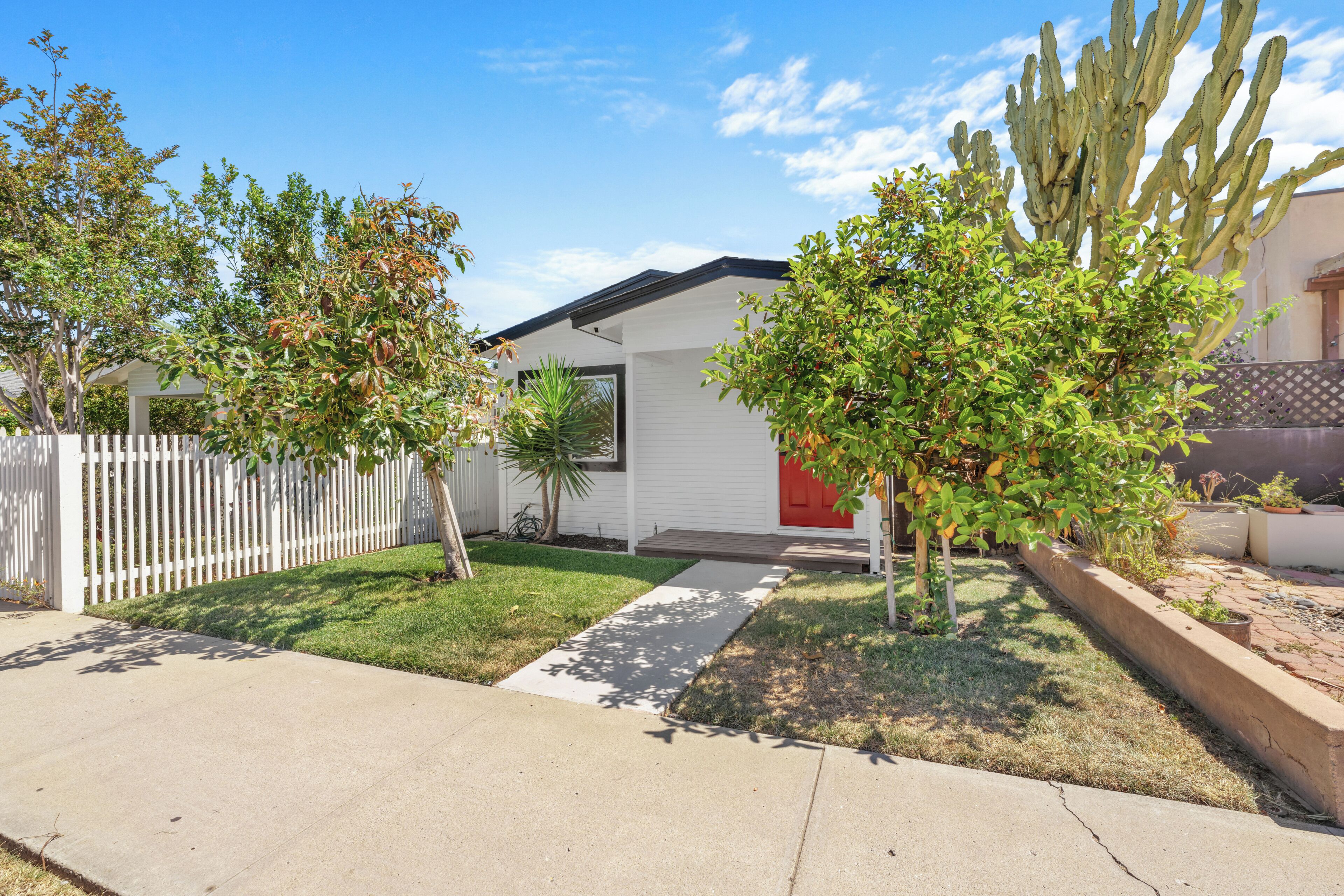 A residential property with a white exterior, a red door, and a fenced yard.