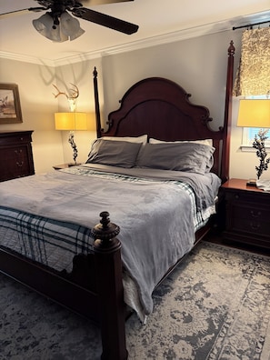 A bedroom with a four-poster bed, a ceiling fan, a lamp, and a decorative deer head on the wall.