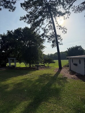 A grassy outdoor area with a gazebo, a large tree, and a small building.