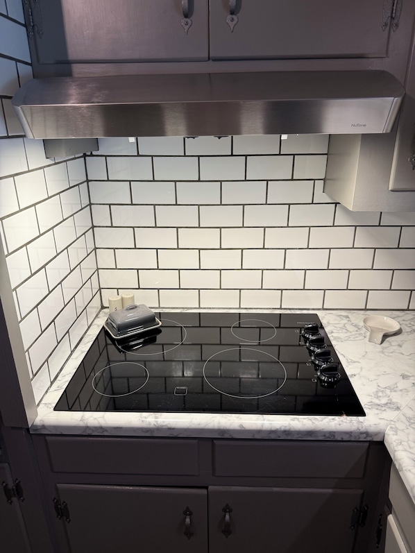 A kitchen with a black stovetop, white tiled backsplash, and dark cabinets.