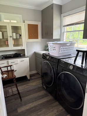 A compact laundry area with a washing machine, dryer, and a chair.