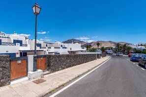 A street with white buildings, a stone wall, and a lamp post. - Villa Marejada by Villa Plus (Playa Blanca)