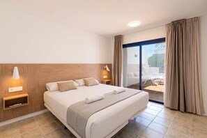 Ein Hotelzimmer mit einem großen Bett, Nachttischlampen, einer Steckdose, einem Fenster mit Vorhängen und Blick auf einen Außenbereich mit Sitzgelegenheiten.