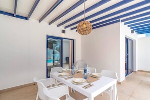 A dining area with a white table set for six, surrounded by white chairs, under a blue-beamed ceiling. - Villa Marejada by Villa Plus (Playa Blanca)