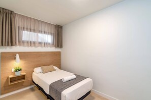 Ein Hotelzimmer mit einem Bett, einem Nachttisch mit Lampe, einer kleinen Pflanze und einem Fenster mit Vorhängen.