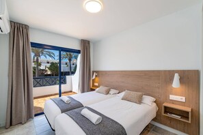 A hotel room with two beds, a wooden headboard, a nightstand, a lamp, and a view of palm trees. - Villa Marejada by Villa Plus (Playa Blanca)