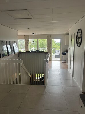 A spacious hallway with a staircase leading to an outdoor deck, a clock on the wall, and a view of greenery outside.